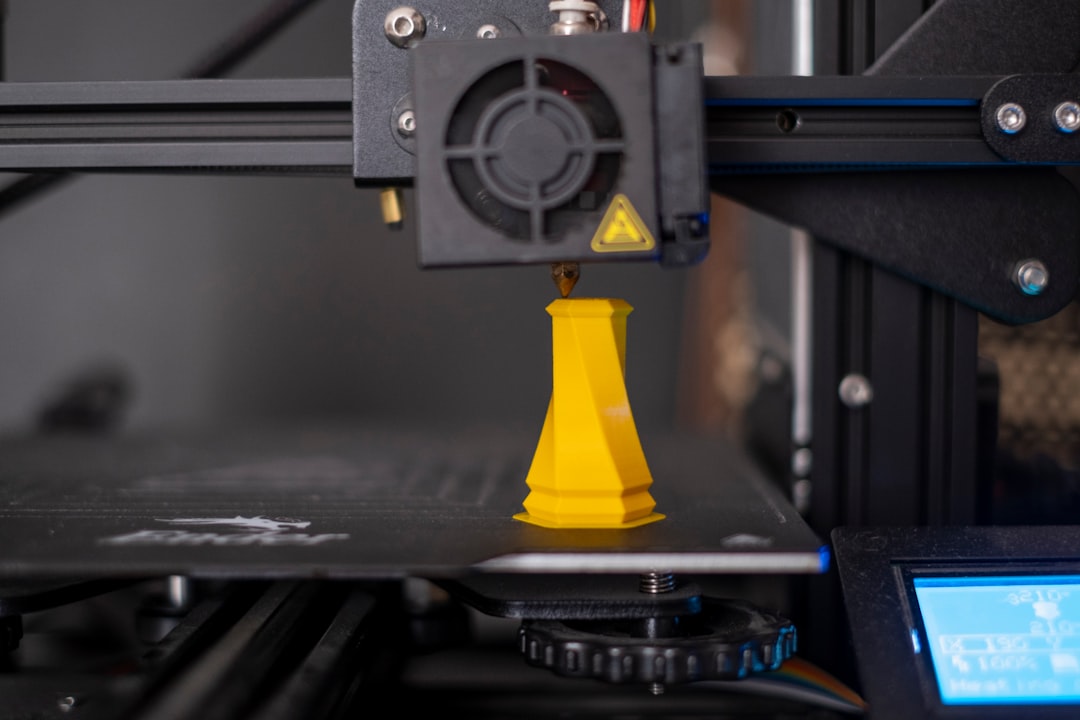 A 3D printer mid-print creating a small yellow geometric object
