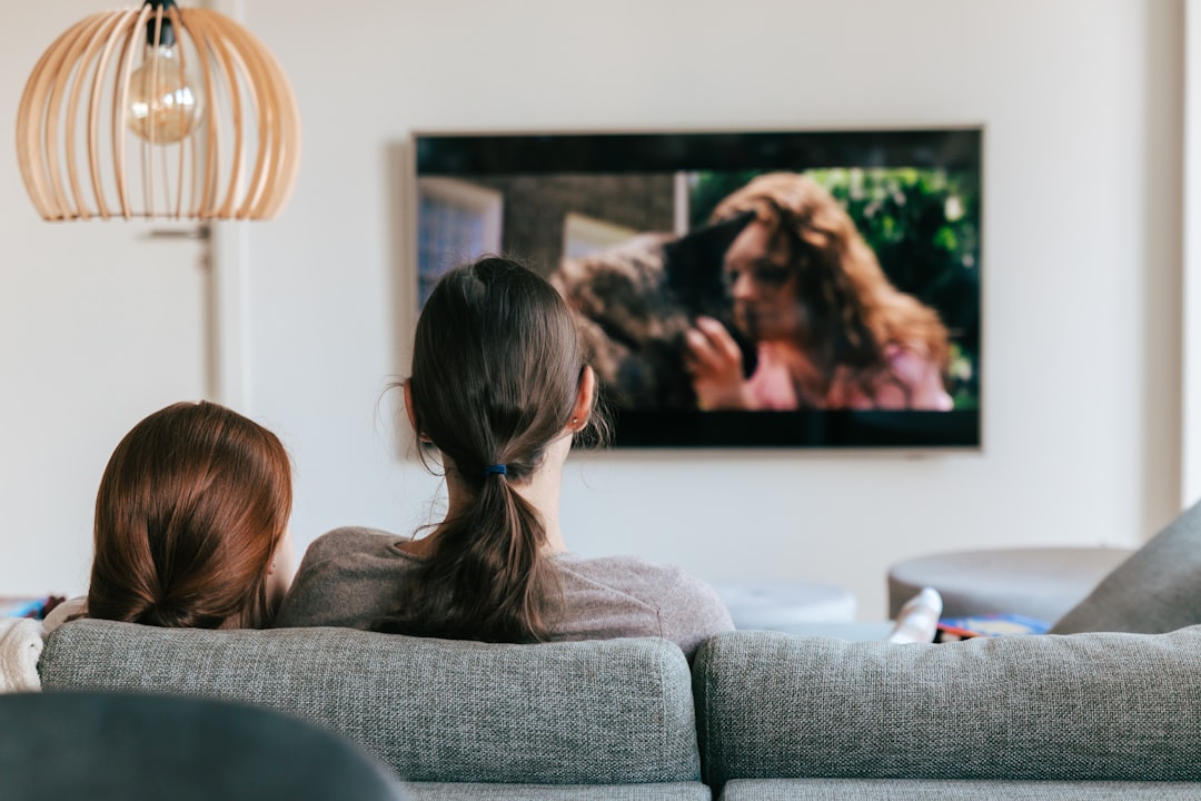 Two people on a couch watching a wall-mounted television in the evening