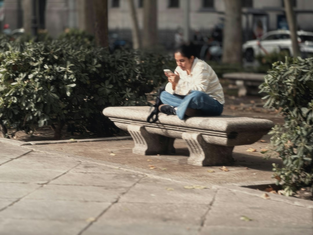Person reading on a phone-sized device while sitting on a park bench