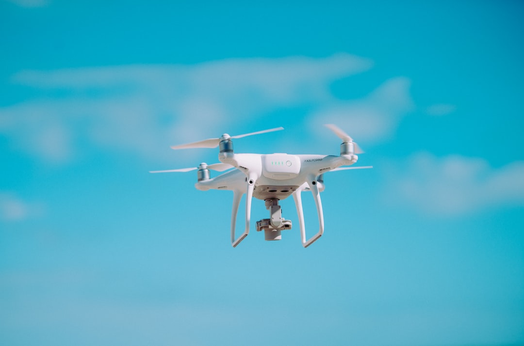 Small quadcopter drone hovering against a blue sky with propellers spinning