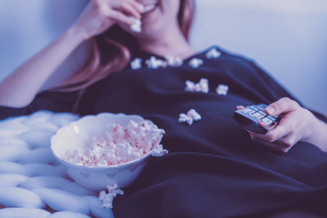 Person relaxing on the couch with popcorn and a remote for movie night