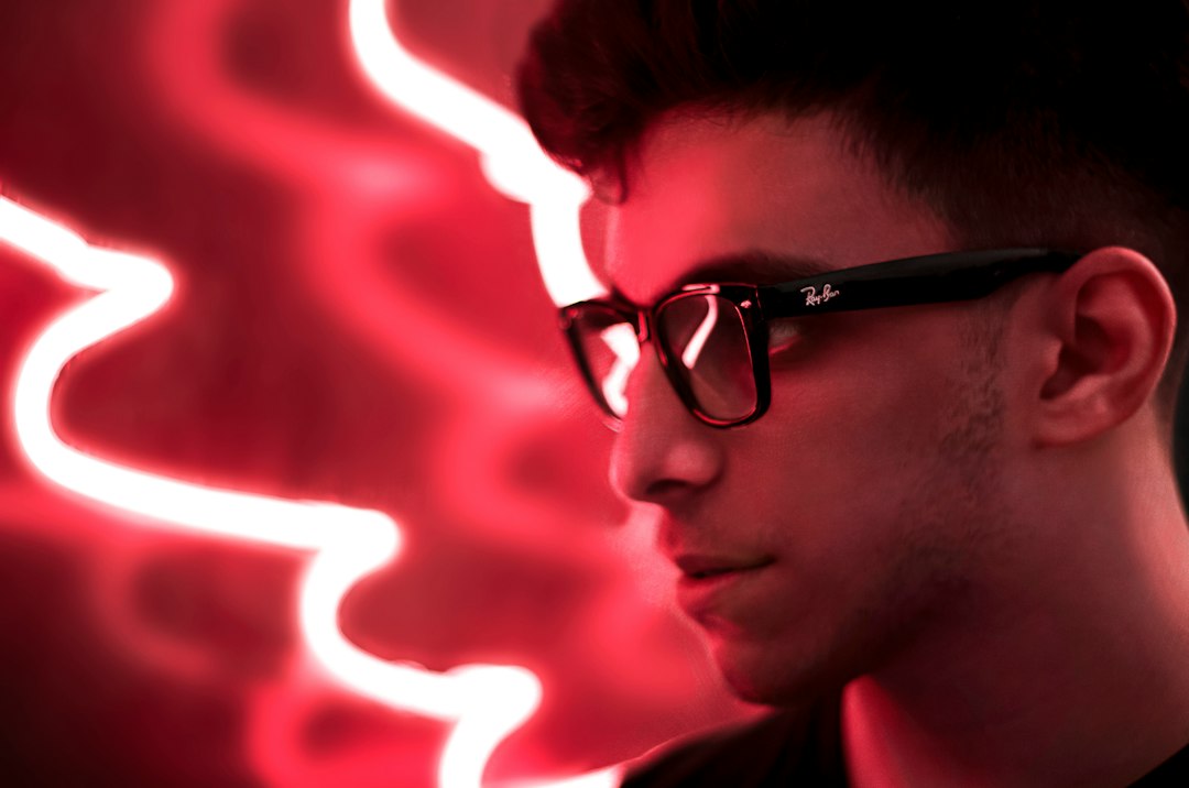 Man wearing glasses with red neon screen glow reflecting in the lenses