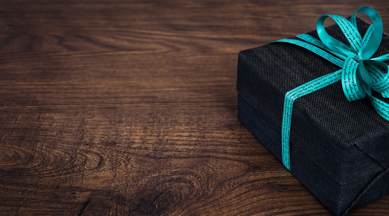 A black gift box tied with a teal ribbon on a wooden table, the kind of small tech gift that fits under fifty dollars