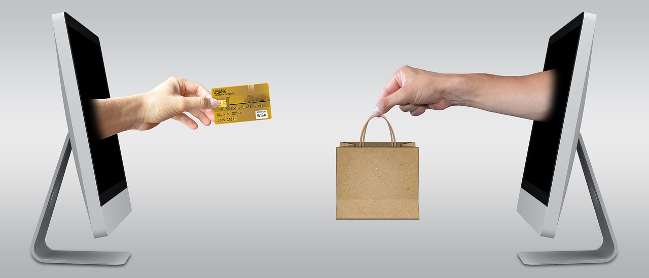 Two monitors facing each other with one hand offering a credit card and the other offering a shopping bag, a picture of online checkout