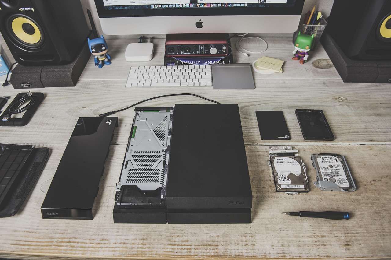 A PlayStation 4 opened up on a wooden desk next to two removed 2.5-inch hard drives and a screwdriver, a reminder of how console storage upgrades used to look