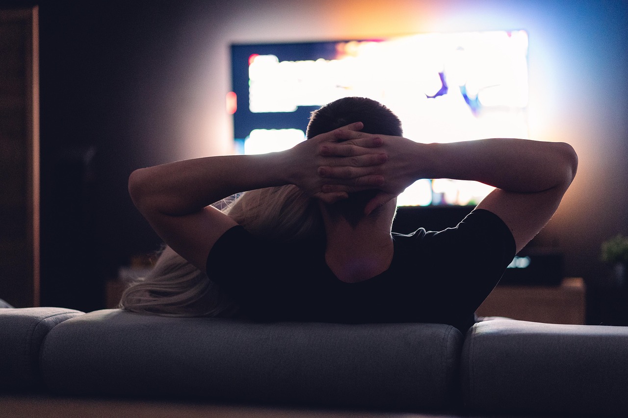 A person relaxing on a couch in a dark living room, watching a bright television, the setup a streaming stick upgrades