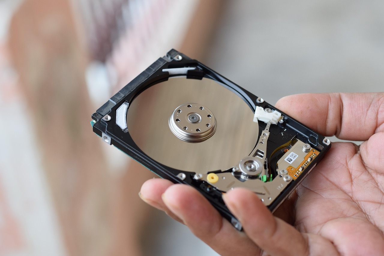 A hand holding an opened 2.5-inch laptop drive, showing the platter inside the casing