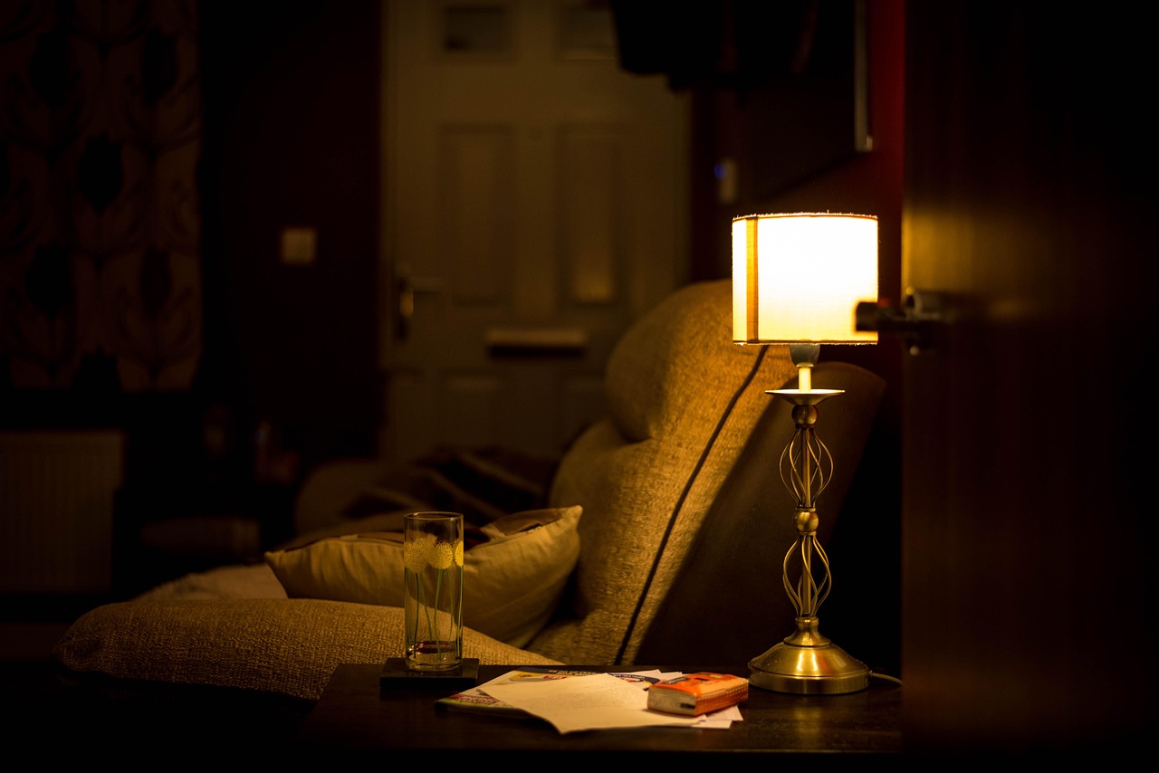 A warm table lamp glowing beside a couch in a dark living room, the kind of lamp a smart plug can switch on at sunset
