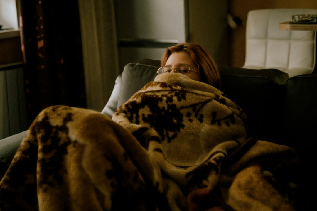Someone buried in a throw on a couch. A lap blanket is the right idea if it is not covering a space heater.