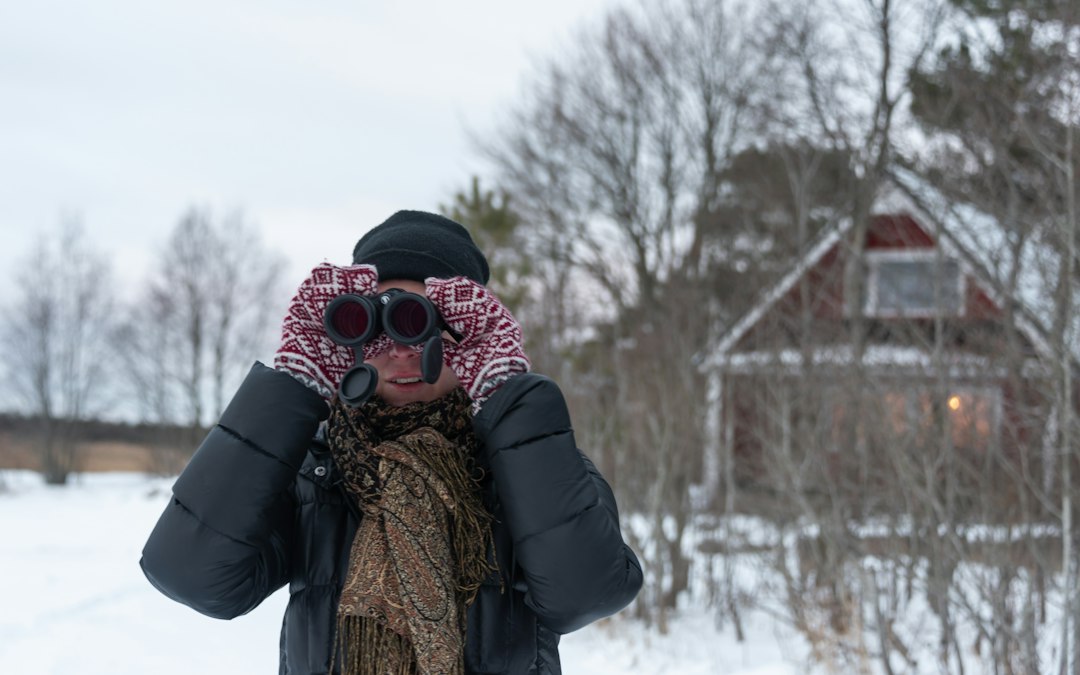 A bundled-up observer holding binoculars to their eyes on a cold night outdoors