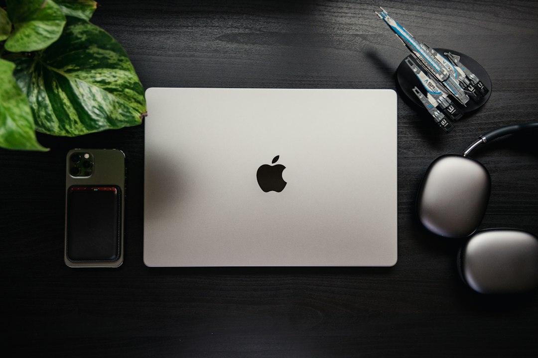 Closed laptop on a dark desk beside a phone and headphones