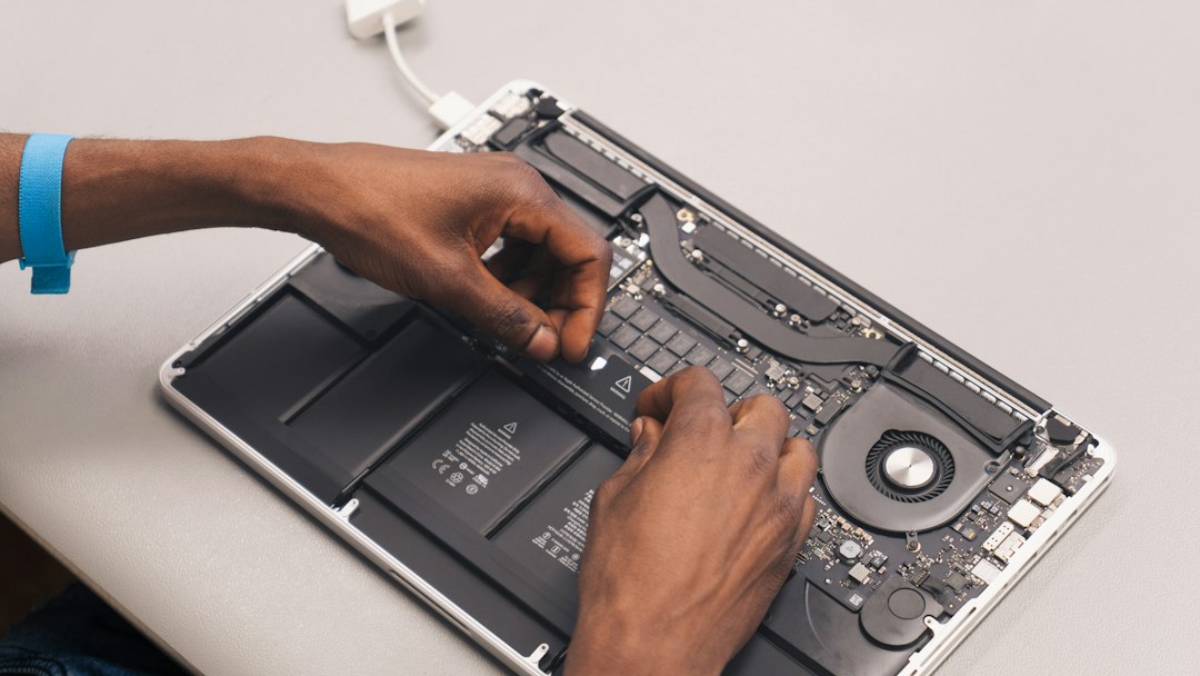 A technician working inside an opened laptop with the battery and logic board exposed, showing where soldered memory lives