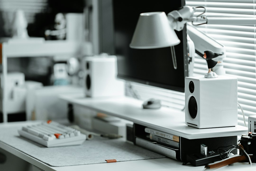 White desktop speakers sitting on a raised monitor shelf above a keyboard