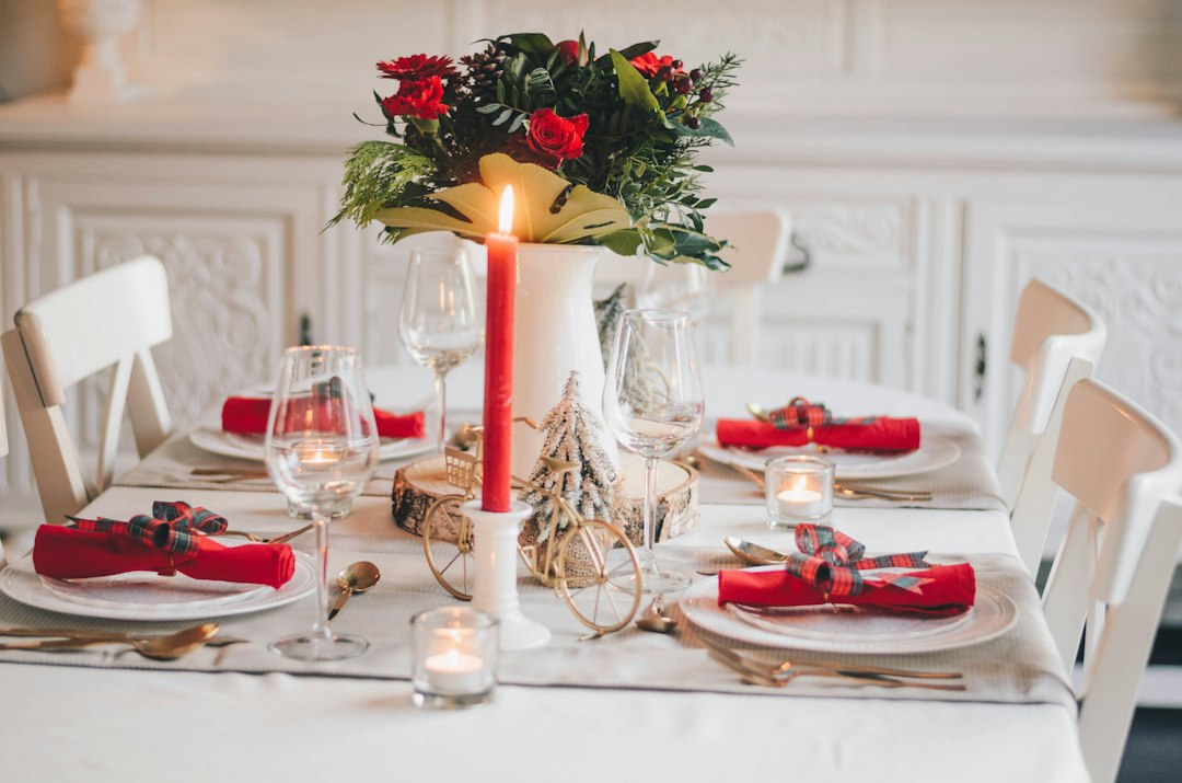A holiday dinner table set with red napkins, candles and a centerpiece of roses and evergreens, with no phones in sight
