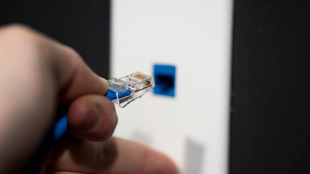 Hand holding an Ethernet plug near a wall jack