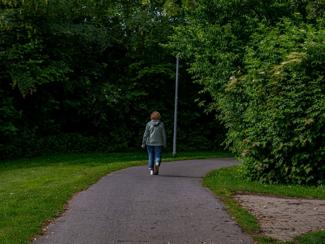 A person walking a quiet park path between dense trees