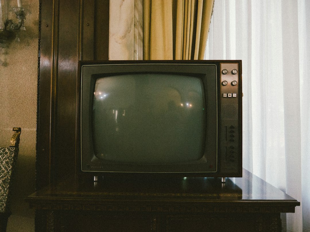 Vintage CRT television with knobs and dials on a wooden stand in a retro room
