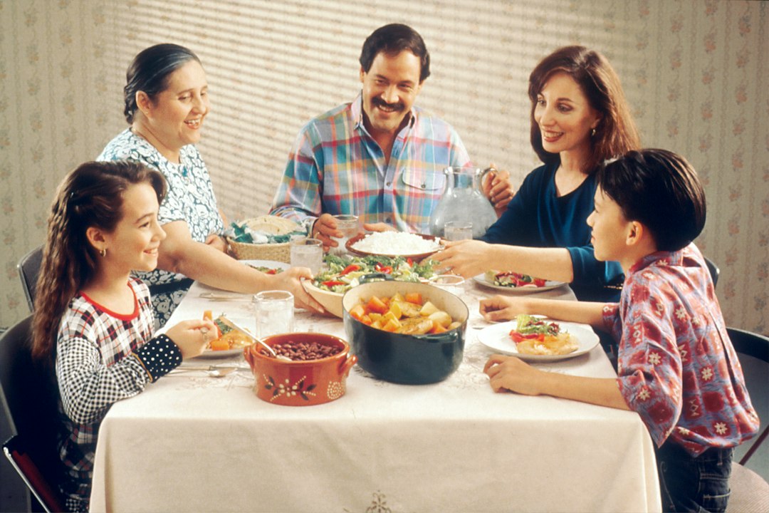 Multi-generational family gathered around a dinner table passing dishes