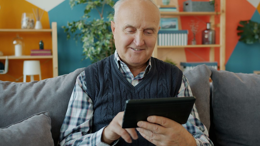 Smiling older man using a tablet on a couch