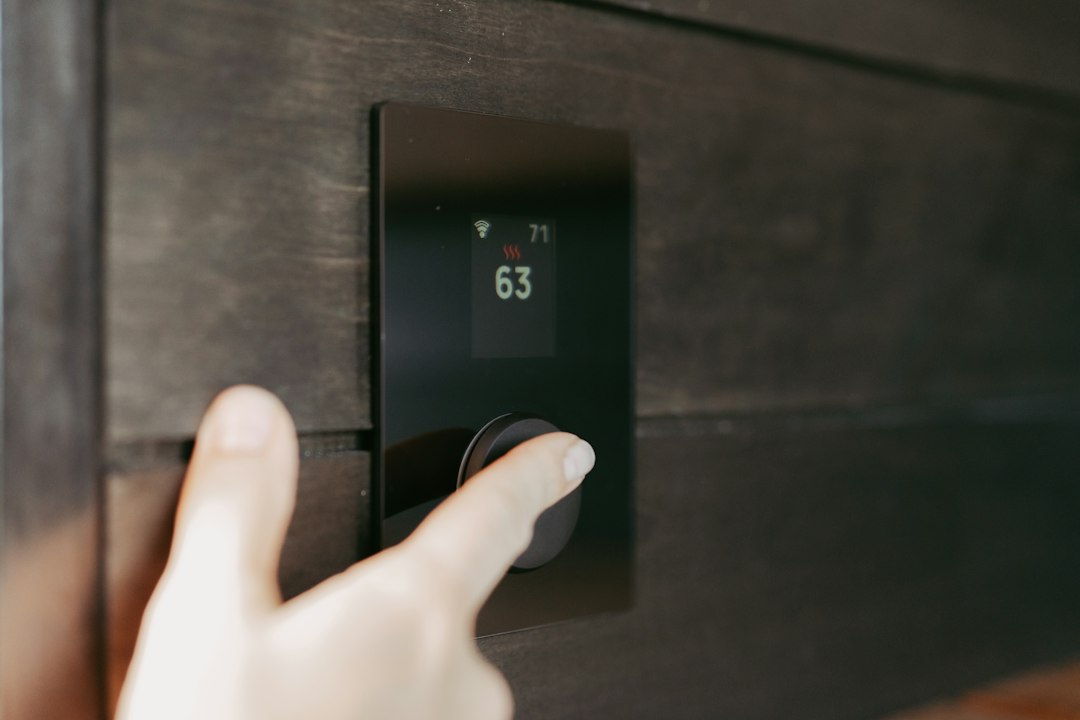 A hand turning the dial on a black digital thermostat set to 63 degrees