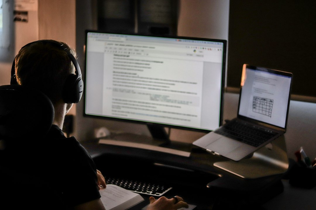 Person working late at a desk with a large monitor and a laptop